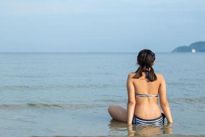Rear view of woman in bikini on beach against sky