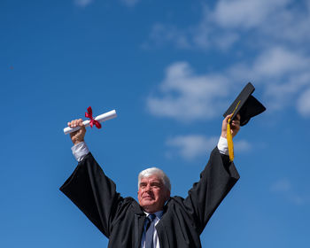 Low angle view of woman with arms raised standing against sky