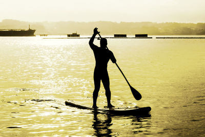 Silhouette man paddleboarding in lake against sky during sunset