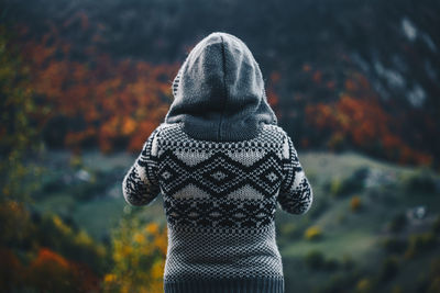 Rear view of woman in sweater standing against trees