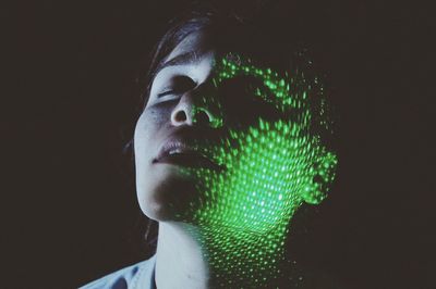 Close-up of shirtless woman with illuminated green lights against black background