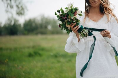 Midsection of woman holding bouquet while standing on field