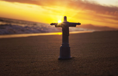 Cross on beach against sky during sunset