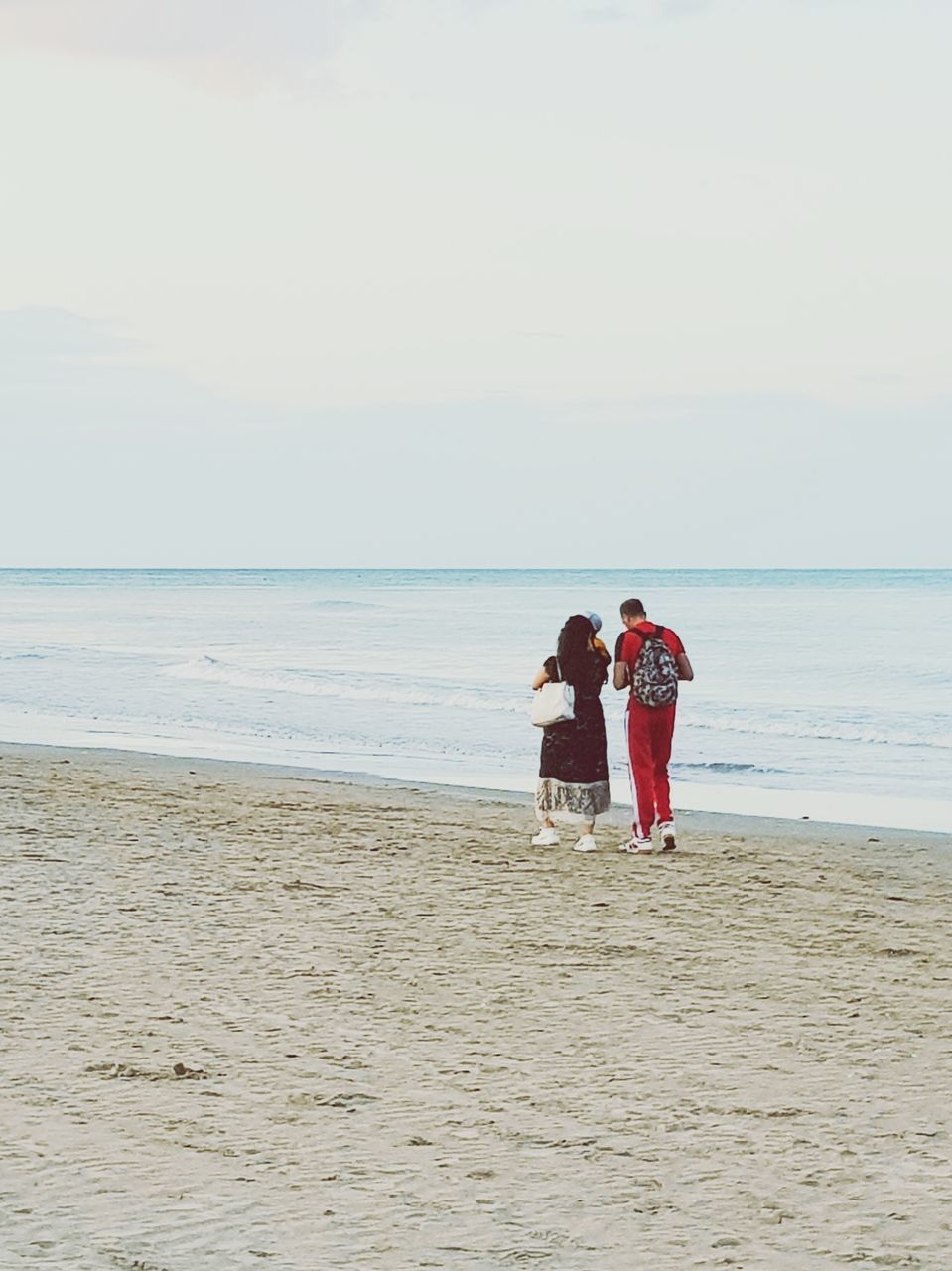 REAR VIEW OF COUPLE ON BEACH AGAINST SEA