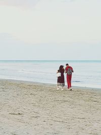 Rear view of couple on beach against sky