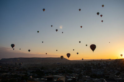 Hot air balloons flying in city against sky during sunset