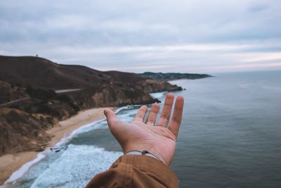 Cropped hand gesturing against sea during sunset