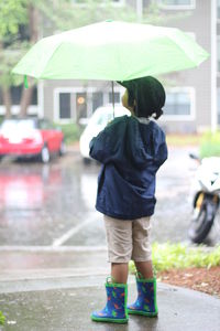 Rear view of boy with umbrella standing on street during rainfall