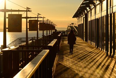 Rear view of woman walking on footpath against sky during sunset