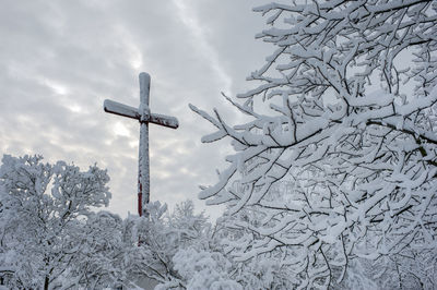 Wooden frozen cross completely covered with snow and icicles and winter landscape under bright sky.