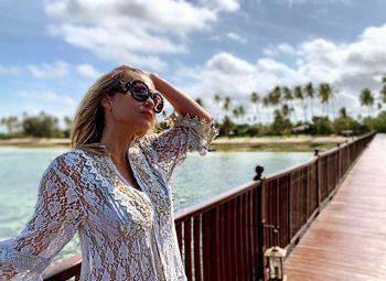 Young woman wearing sunglasses while standing on pier against sky