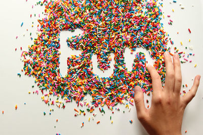 Cropped hand making fun text amidst colorful sprinkles over white background