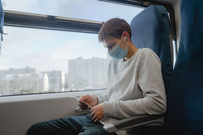 Young man wearing mask sitting by train window