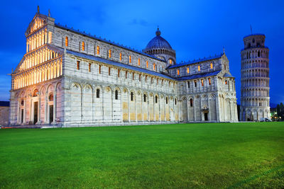 Illuminated pisa cathedral by leaning tower against blue sky at dusk