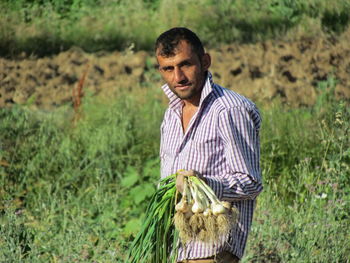 Portrait of farmer holding scallions while standing on agricultural field