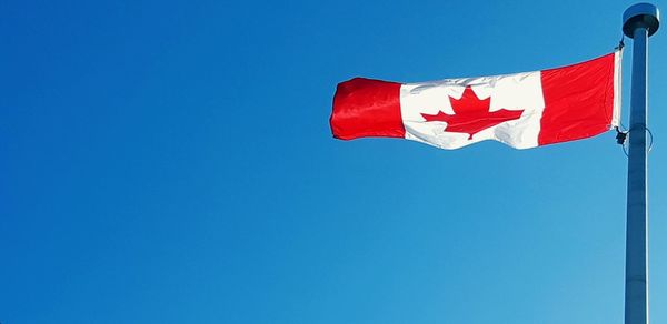 Low angle view of flag against clear blue sky