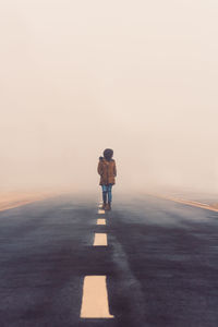 Rear view of boy standing on road against clear sky