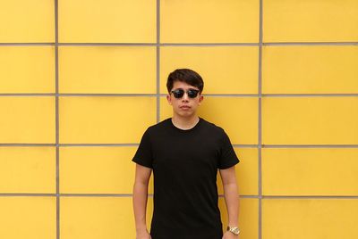 Portrait of young man standing against yellow wall