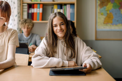 Smiling girl holding digital tablet in classroom