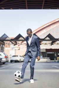 Young businessman playing with soccer ball at parking lot on sunny day