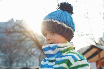 Boy looking away while standing against sky during winter