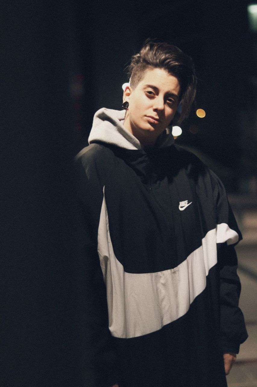 PORTRAIT OF YOUNG MAN STANDING AGAINST DARK