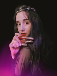 Portrait of beautiful young woman holding lipsticks against black background