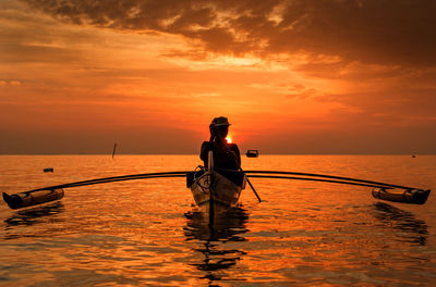 Man standing on boat in sea against sky during sunset