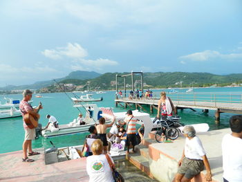 People sitting on sea by mountains against sky