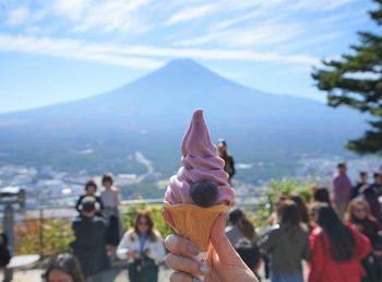 Cropped hand of woman holding ice cream against mountain