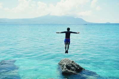 Rear view of man jumping in sea against sky