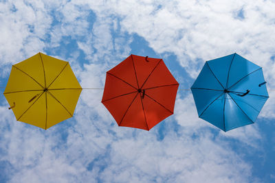 Low angle view of multi colored umbrellas hanging against sky