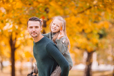 Portrait of father carrying daughter on back during autumn at park