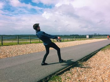 Full length of young man bending on road against cloudy sky during sunny day