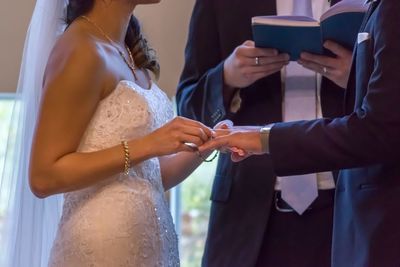 Midsection of bride putting ring in groom finger at wedding