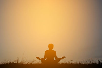 Silhouette woman practicing yoga on field against sky during sunset