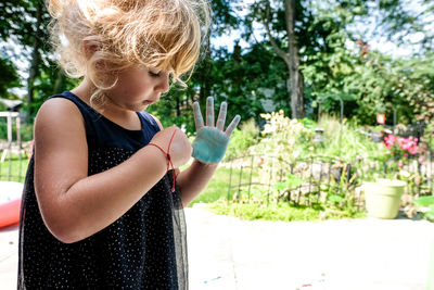 Little girl coloring with chalk on hands outside in sunlight