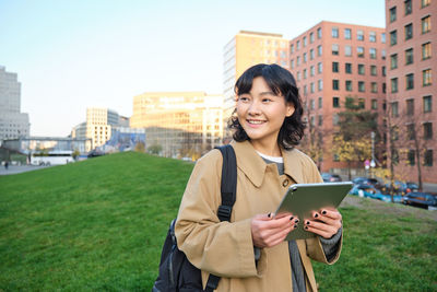 Portrait of young woman using mobile phone while standing against trees