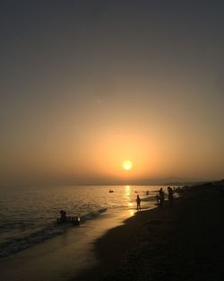 Silhouette people on beach against sky during sunset