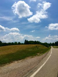 Road passing through field against cloudy sky