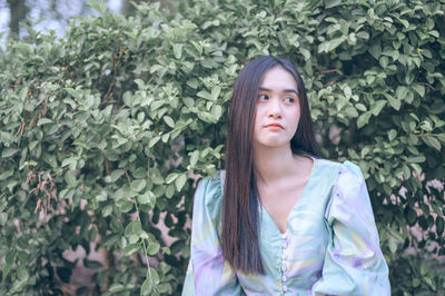 Portrait of young woman standing against plants