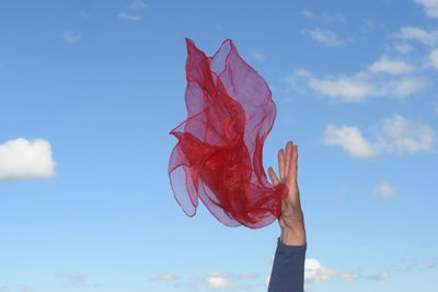 Low angle view of person holding textile against blue sky