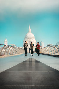 People walking in front of historic building against sky