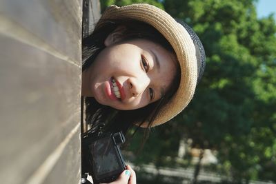 Portrait of young woman with camera peeping from door