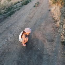 High angle view of girl sitting in hat on road. 