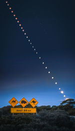 Low angle view of illuminated sign against sky at night