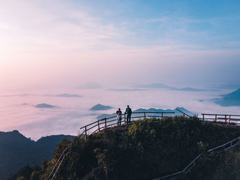 People standing by railing against sky during sunset