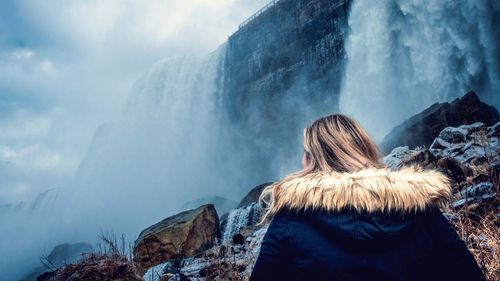 Rear view of woman wearing fur coat standing against waterfall