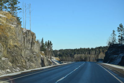 Empty road by trees against clear blue sky