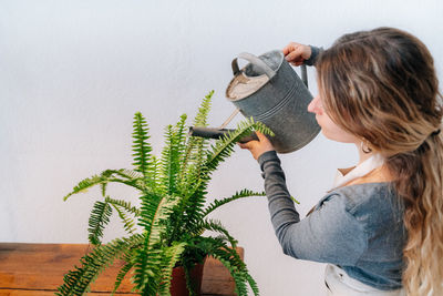 Rear view of woman holding potted plant against wall